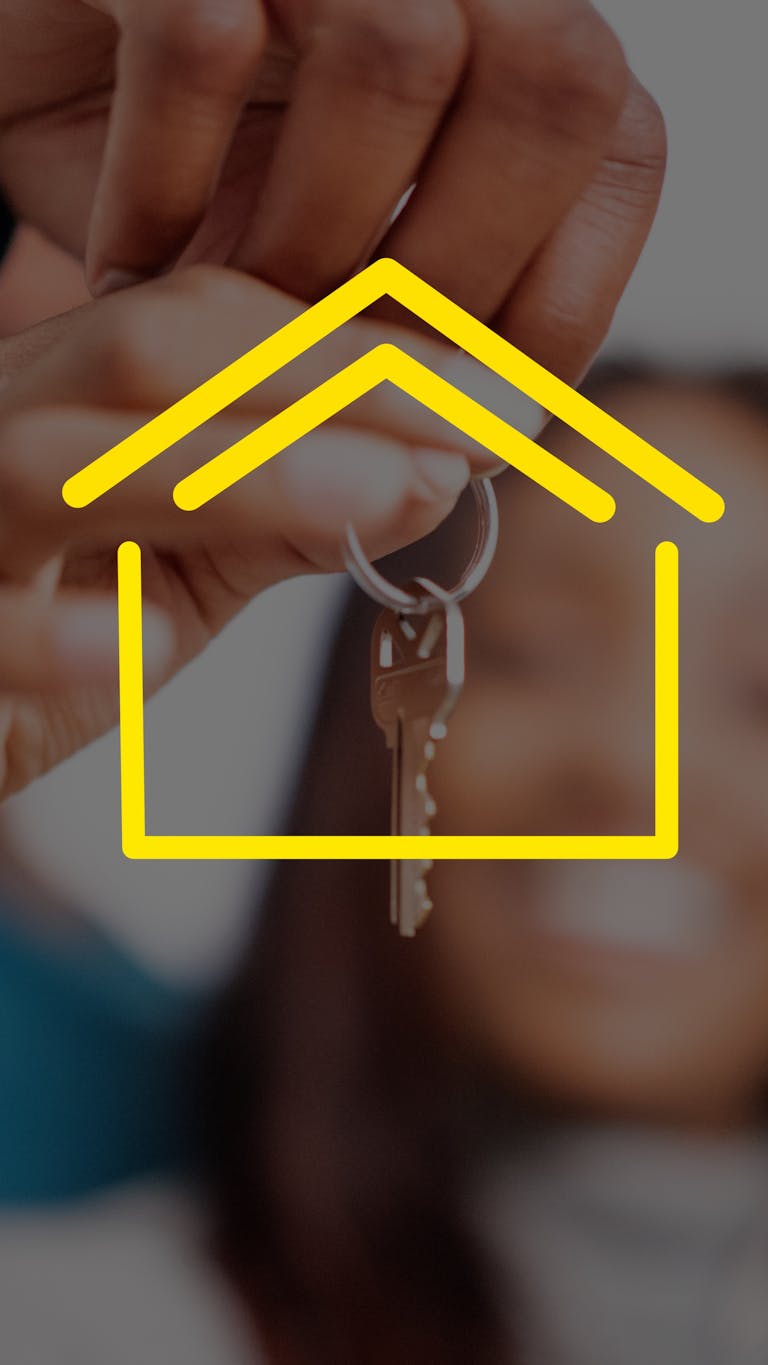 Close-up of hands holding house keys with yellow house icon overlay, representing real estate.